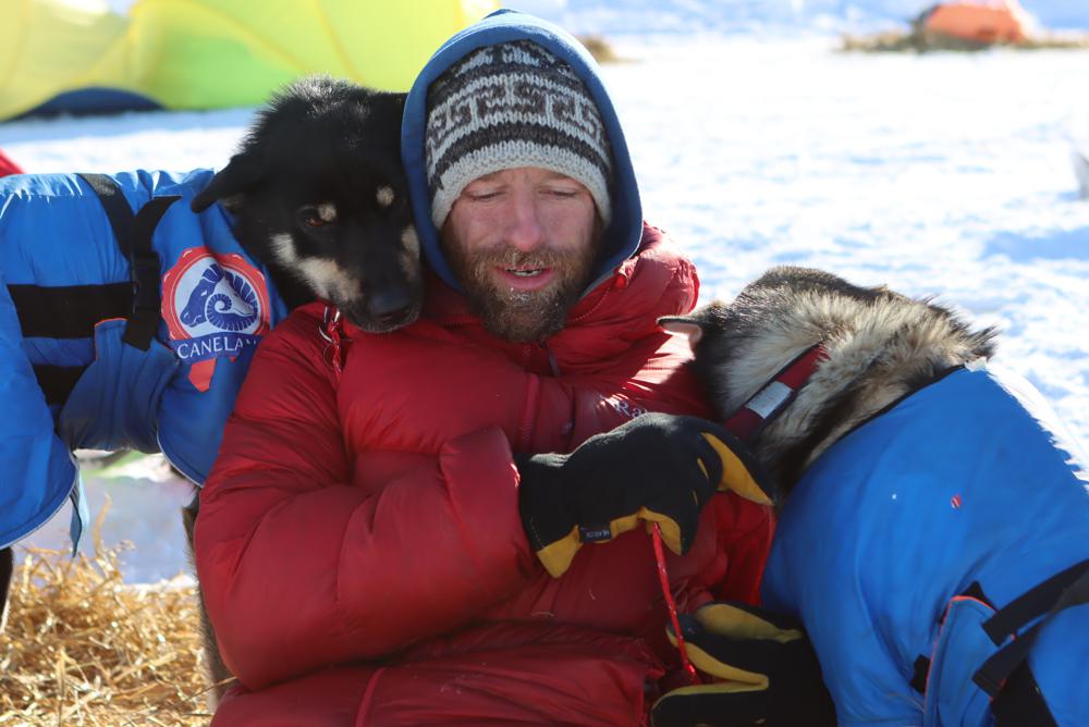 Musher Jessie Holmes takes a break from cooking his dogs a meal to nuzzle with two wheel dogs at the Ophir checkpoint during the Iditarod Trail Sled Dog Race on March 10, 2021, in Alaska. The television star and Iditarod musher sustained injuries this week when helping clean up storm damage along the Bering Sea coast.